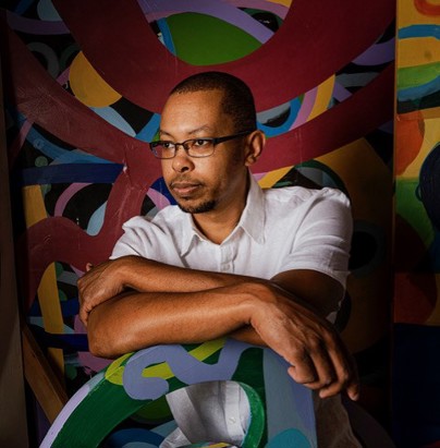 Artist Jamal Barber seated with artwork in the background