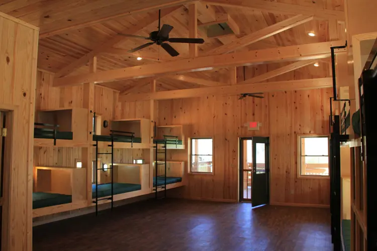 The image depicts the inside of a camp cabin including wood floors and walls, and built in bunk beds.