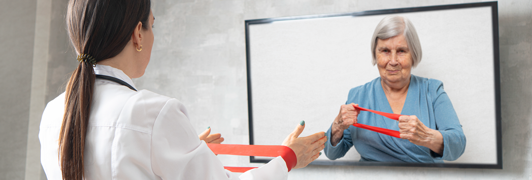 A physician with her back to the camera showing a patient via telehealth, displayed on a tv screen how to use a red exercise band 
