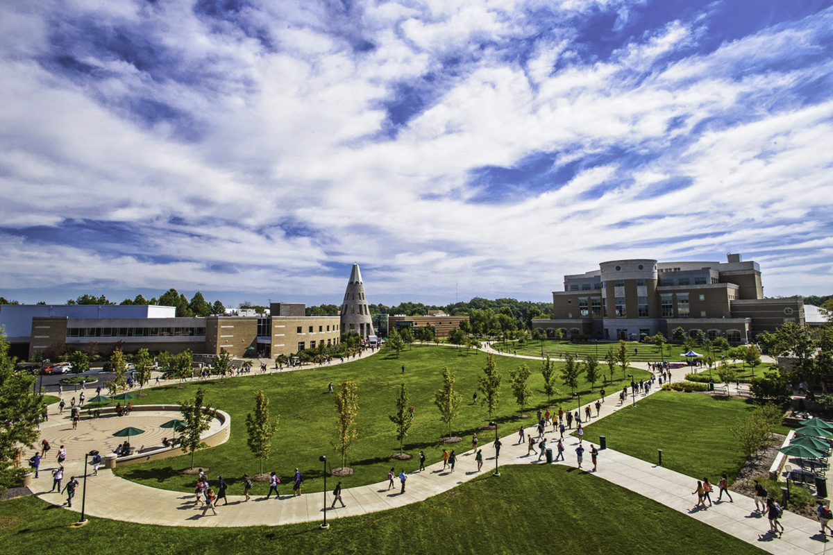 A wide shot of The Quad featuring the University Center and Rice Library with students walking by.