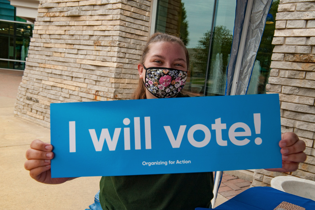 Image of a student encouraging others to vote at a tabling event holding a sign that says I will vote.