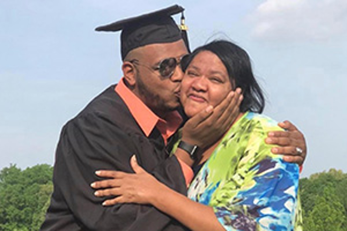 USI graduate Willie Sanders, in his cap and gown, gives a woman a kiss on the cheek.
