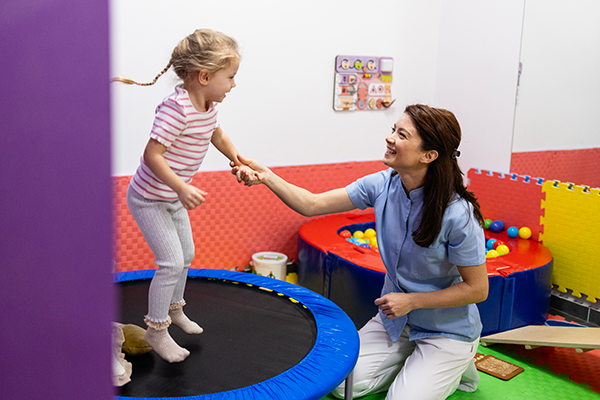 OT helping child jump on a small trampoline