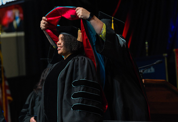Grad student receives her masters hood on stage at commencement.
