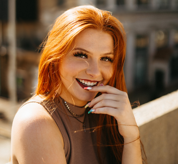 Elizabeth Kershaw standing on a rooftop, she has long red hair and is wearing a brown sleeveless top