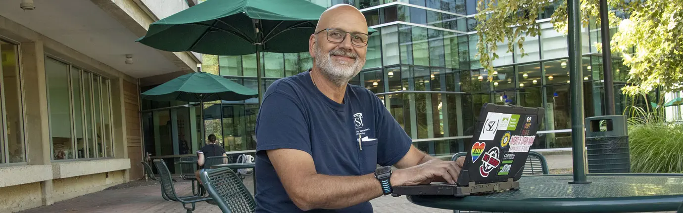 Adult learner smiles at the camera while working on his laptop on the USI campus