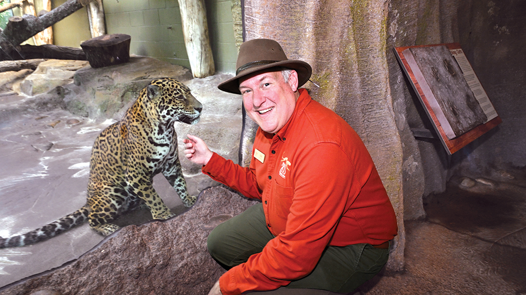 man in jungle hat sitting next to jaguar