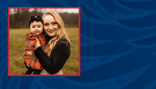 Blonde female holding a baby in a field with trees