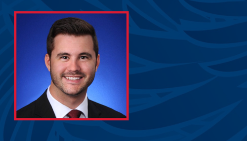 Ryan Hadley portrait: white man with dark brown hair and facial hair wearing white collared shirt with red tie and black suit jacket