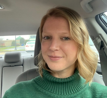 Caroline Jalain wearing a green turtleneck sweater sitting in her car