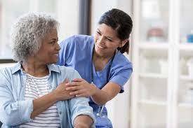 A nurse standing behind a geriatric patient, holding her hand
