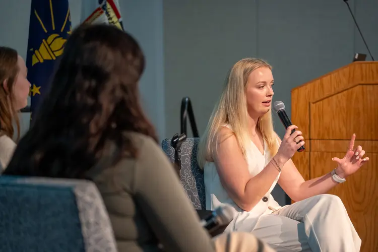 Social media symposium speaker Kaylee Johnson speaks into the microphone while seated with students