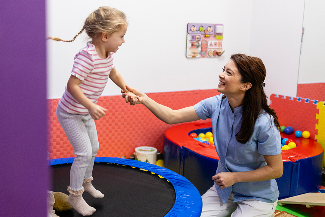 OT helping child jump on a small trampoline