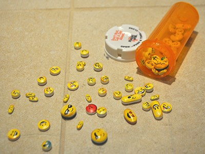 Pill bottle and various pills with emojis on them