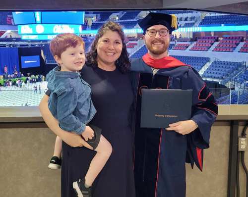 Dr Schaefer in commencement dress holding his diploma with his family