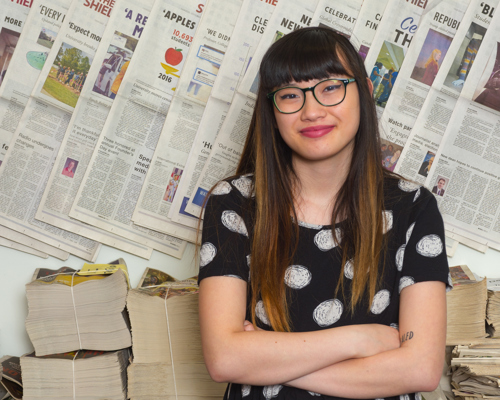 Gabrielle Wy standing in front of copies of newspaper