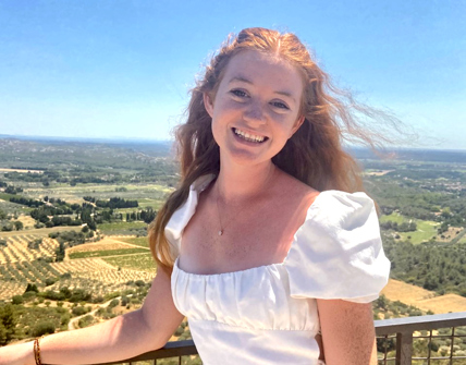 Caitlin Daymon stands on a balcony overlooking farm fields in a foreign country