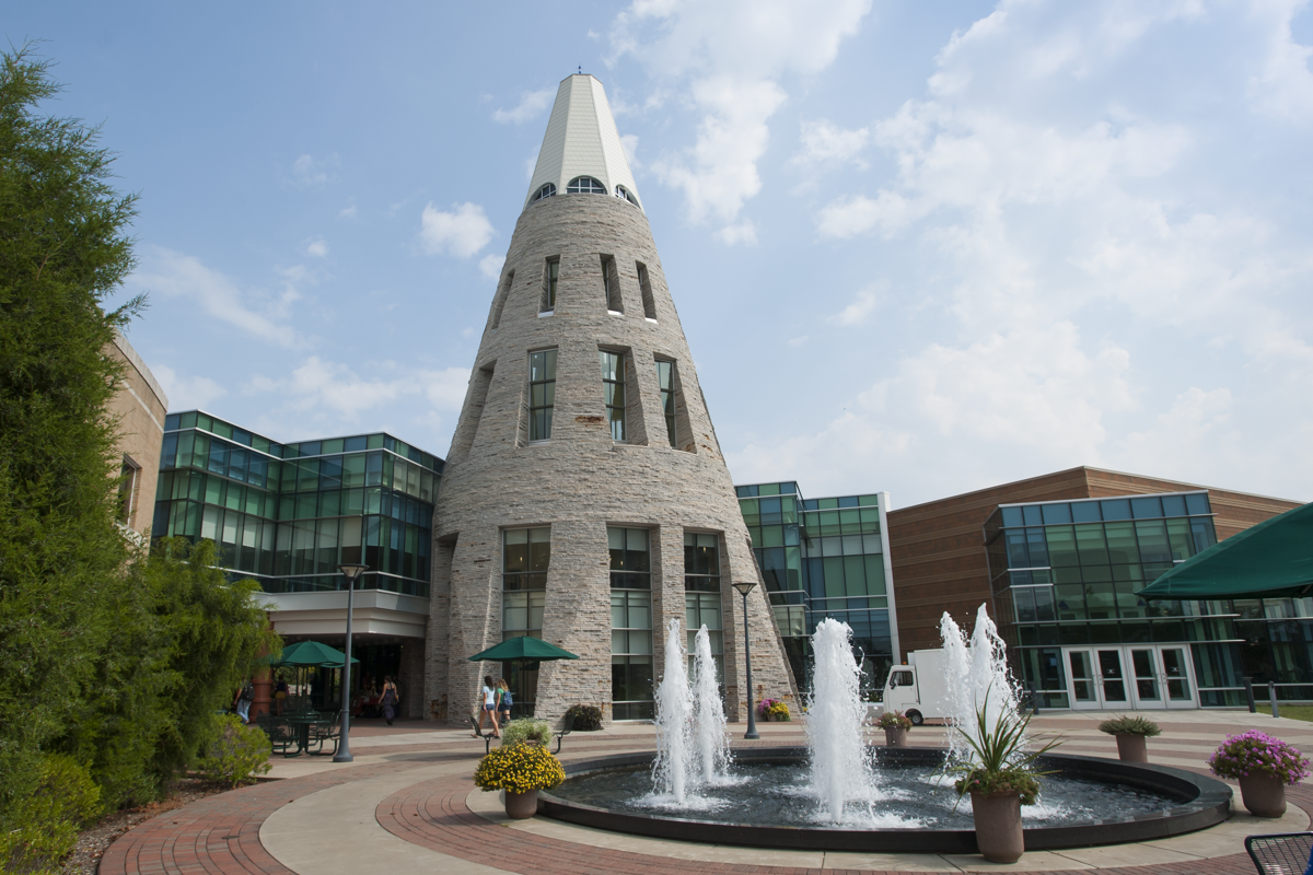 The Cone and the fountain are featured in the center of the photo. It is a sunny day on campus, and two students are walking under the UC Breezeway.