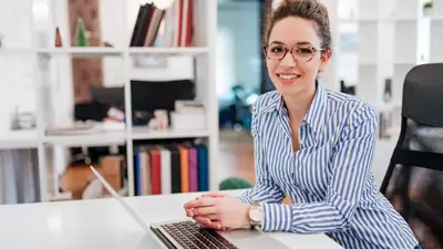 Online student smiles at the camera in front of her laptop