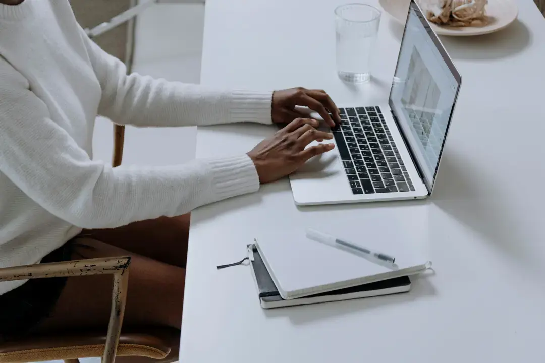 Person working on a laptop at a clean desk with a notebook, pen, and glass of water