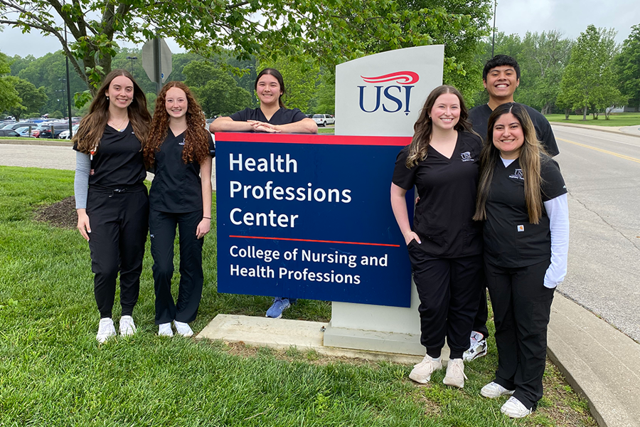 Graduating Respiratory Therapy students pose together in scrubs by the Kinney College of Nursing and Health Professions sign